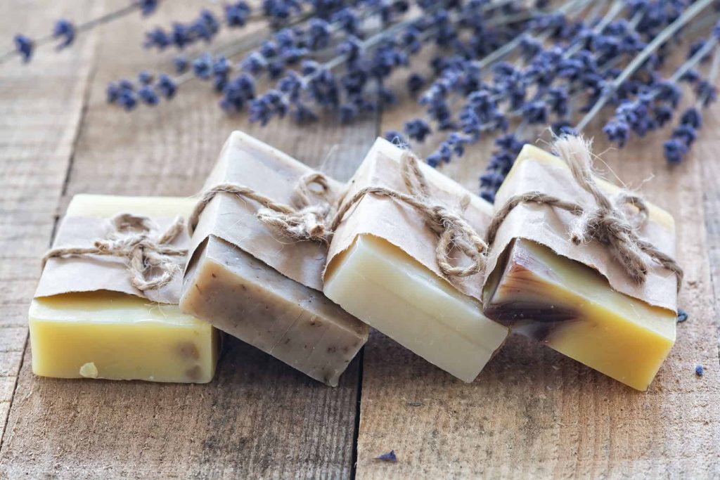 Four bars of Handmade Soap on a wooden board and lavender in the distance