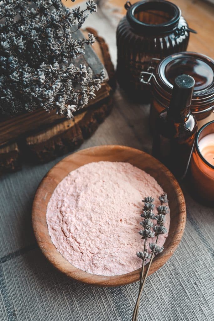 Picture of pink cosmetic clay in a wooden bowl surrounded by lavender. 